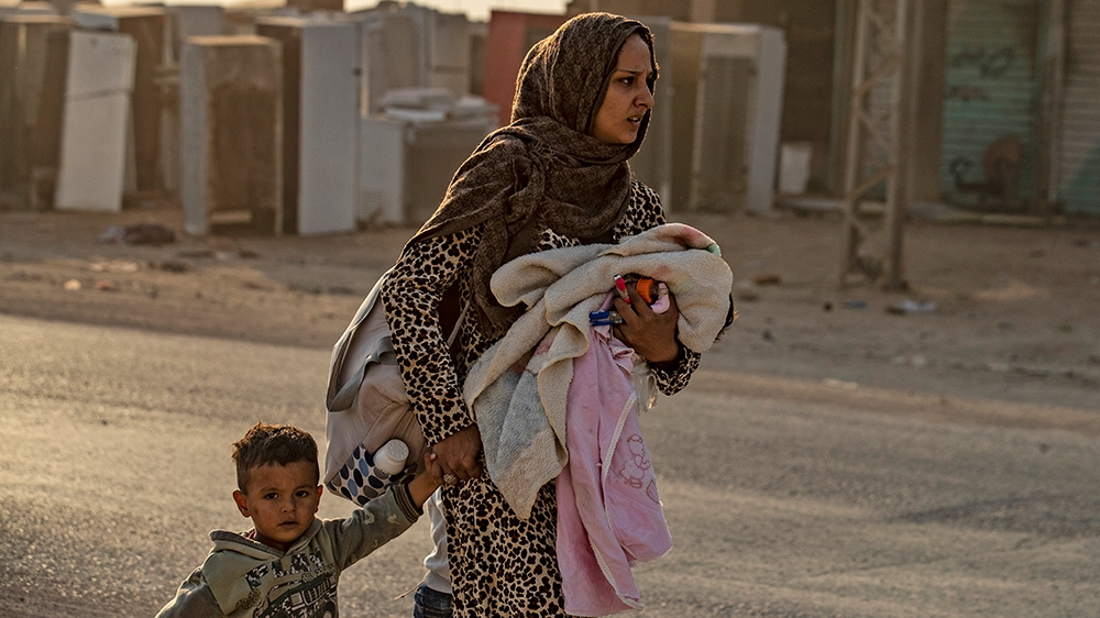 A woman flees with her children amid Turkish bombardment on Syria's northeastern town of Ras al-Ain in the Hasakeh province along the Turkish border on October 9, 2019. - Turkey launched a broad assau