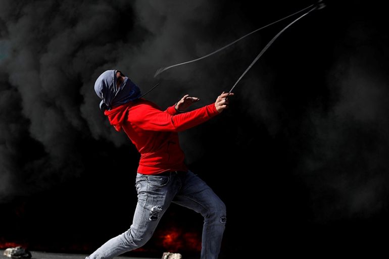 A demonstrator hurls stones at Israeli troops during a protest as Palestinians call for a day of rage over U.S. decision on Jewish settlements, near the Jewish settlement of Beit El in the Israeli-occ