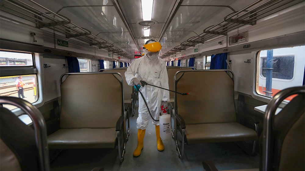 An employee in protective gears sprays disinfectant in the wake of coronavirus outbreak inside a train at the Senen train station in Jakarta Indonesia, Sunday, March 15, 2020. Indonesia's capital city