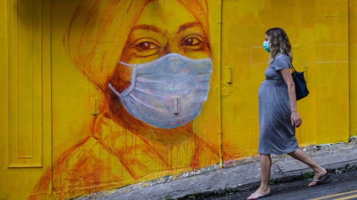 A pregnant woman wearing a face mask as a precautionary measure walks past a street mural in Hong Kong, on March 23, 2020, after the city’s Chief Executive announced plans to temporarily ban the sale