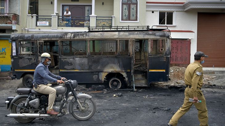 A policeman rides past a burnt police vehicle in Bangalore on August 12, 2020, after violence broke out overnight in Devara Jevana Halli area following a "derogatory" Facebook post about the Prophet M