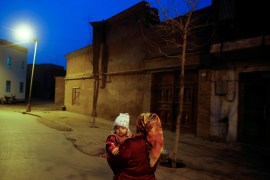 A woman carries a child at night in the old town of Kashgar, Xinjiang Uighur Autonomous Region, China, March 23, 2017 [File: Thomas Peter/ Reuters]