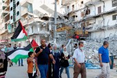 Protesters in Gaza City wave Palestinian flags while marching past a building destroyed by an Israeli air raid last month [Adel Hana/AP Photo]