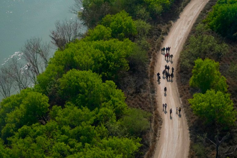 A group of people walks down a winding unpaved road next to the Rio Grande River.