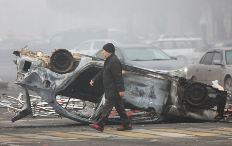 A man walks past a car that was torched during protests in Almaty, Kazakhstan