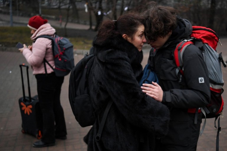 People hug as a woman with a suitcase uses her smartphone outside a metro station in Kyiv