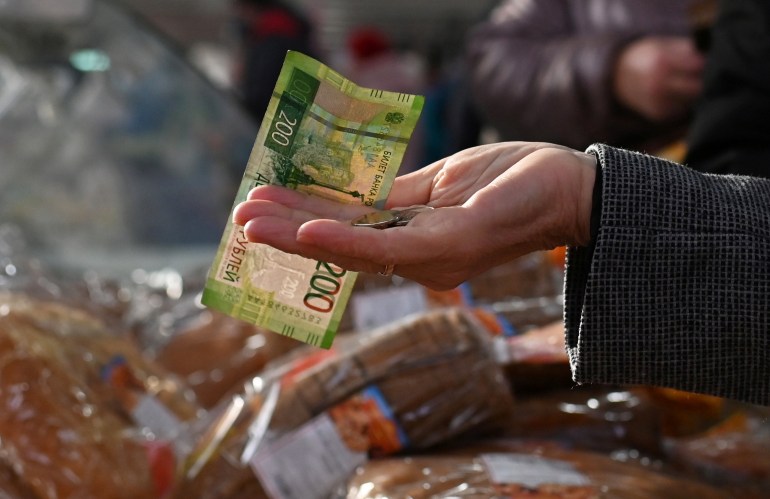 A customer is seen handing over Russian rouble banknotes and coins to a vendor at a market in Omsk, Russia