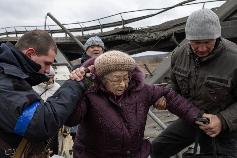 People help a woman to cross a destroyed bridge in the town of Irpin outside Kyiv, Ukraine.