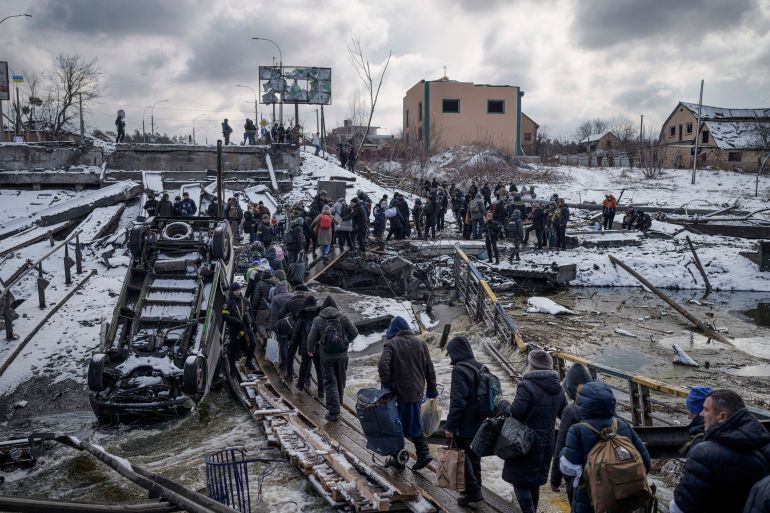 Ukrainians cross an improvised path under a destroyed bridge while fleeing Irpin, in the outskirts of Kyiv