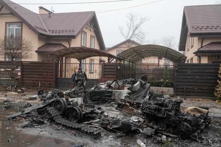 A Ukrainian soldier checks a destroyed Russian tank in front of pink-coloured houses, in Irpin, close to Kyiv, 