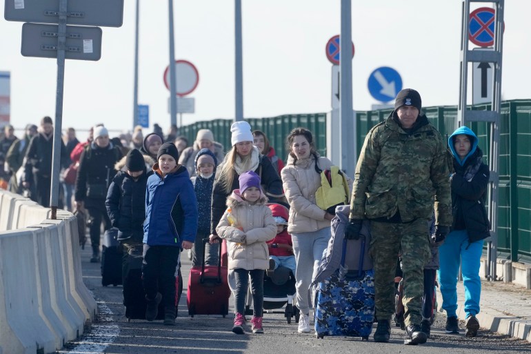 A Polish border guard assists refugees from Ukraine as they arrive to Poland at the Korczowa border crossing, Poland, Saturday, Feb. 26, 2022.