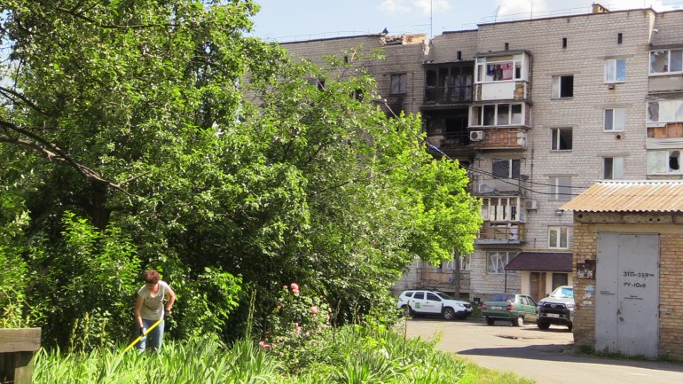 A Ukrainian woman tending her garden near a shelling-damaged apartment building in Makariv