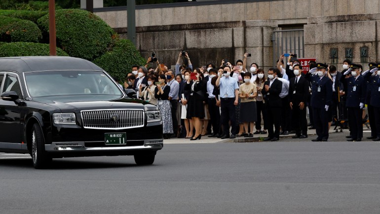 People stand on the street outside Japan's parliament as the hearse carrying Shinzo Abe's body passes