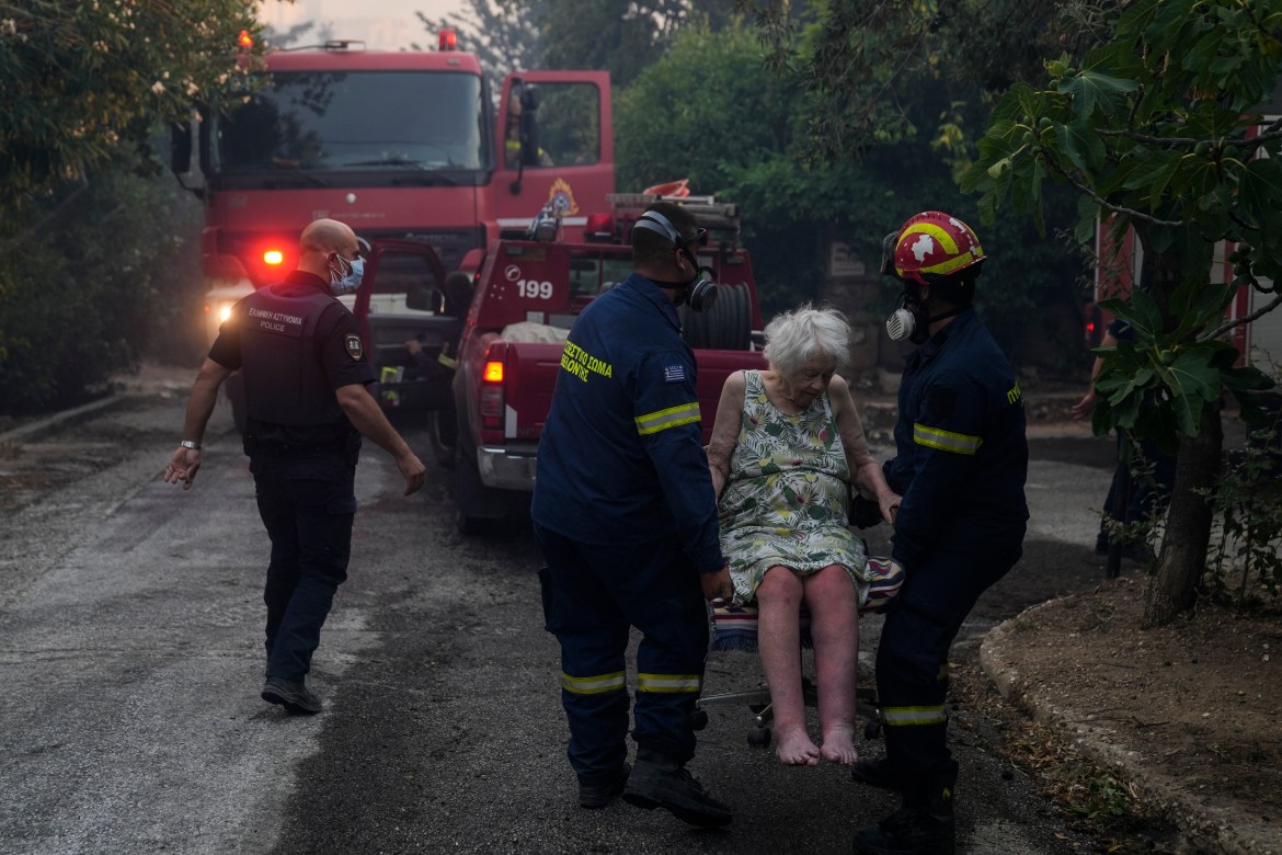 Firefighters evacuate an elderly woman from her house in Penteli,