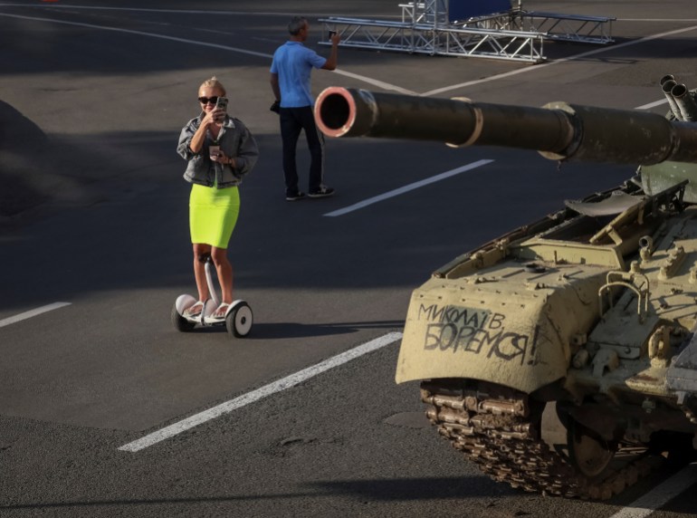 A woman rides on a scooter near a destroyed Russian tank located on a main street in Kyiv, Ukraine.