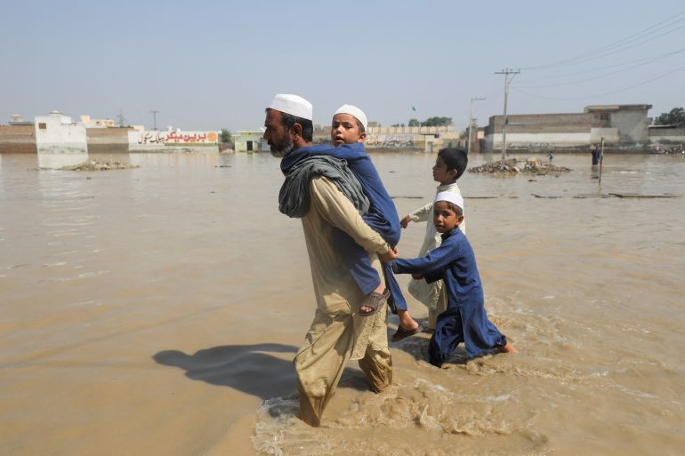 A man walks with children amid flood water along a road, following rains and floods during the monsoon season in Nowshera, Pakistan on August 30, 2022 [Fayaz Aziz/Reuters]