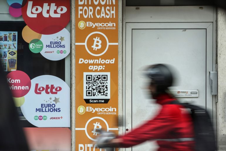 Bitcoin and the Byecoin app advertised in the window of a store in Antwerp, Belgium with blurred (for motion) man cycling past