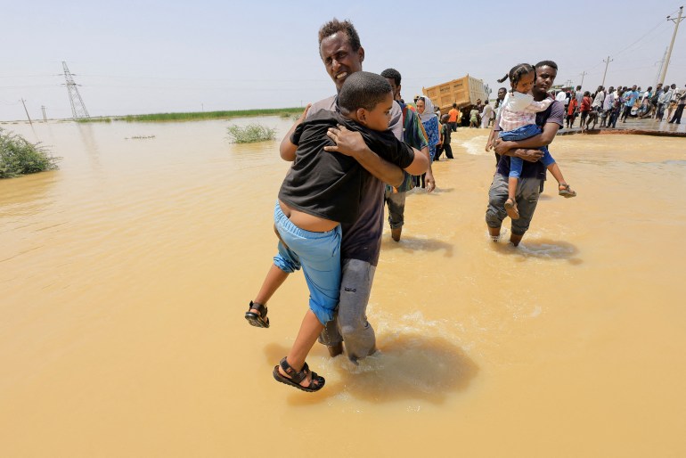 People cross the water during a flood in Al-Managil locality in Gezira state