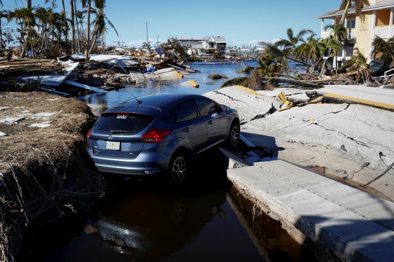 A car on a destroyed road surrounded by water and fallen trees after Hurricane Ian in Florida