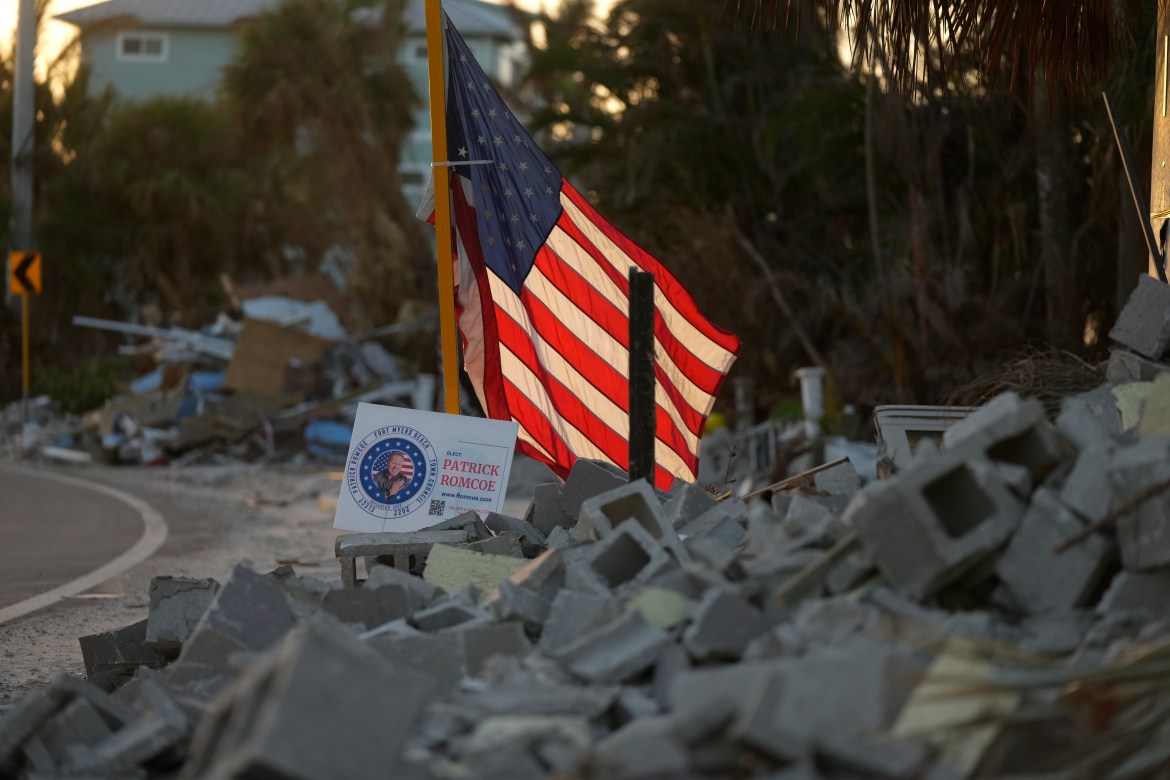 A signs promoting a candidate for Fort Myers Beach town council sits amid debris near an American Flag.