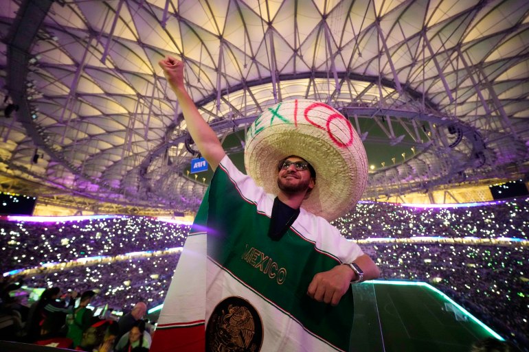 Karima Mohammed of Egypt cheers on Mexico with a raised fist as wears a sombrero with the letters Mexico written on it and a Mexican flag drapes his body.