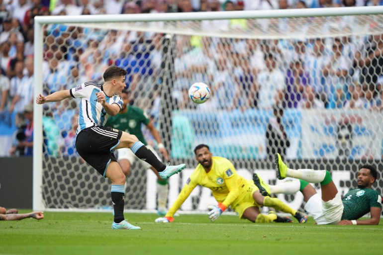 An Argentinian shoots in the Argentina v Saudi Arabia match as the Saudi goalkeeper and a defender, sprawled out on the pitch, look up at the ball.