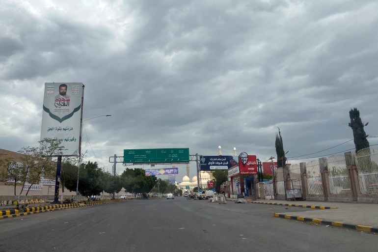 A poster featuring the founder of the Houthi movement on the left side of a road, on the right, a sign for KFC