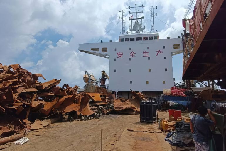 A view from the bow of the Chinese-registered vessel after it was seized. There is rusty scrap metal piled on the deck. The bridge is white and has Chinese characters painted in red across the top.
