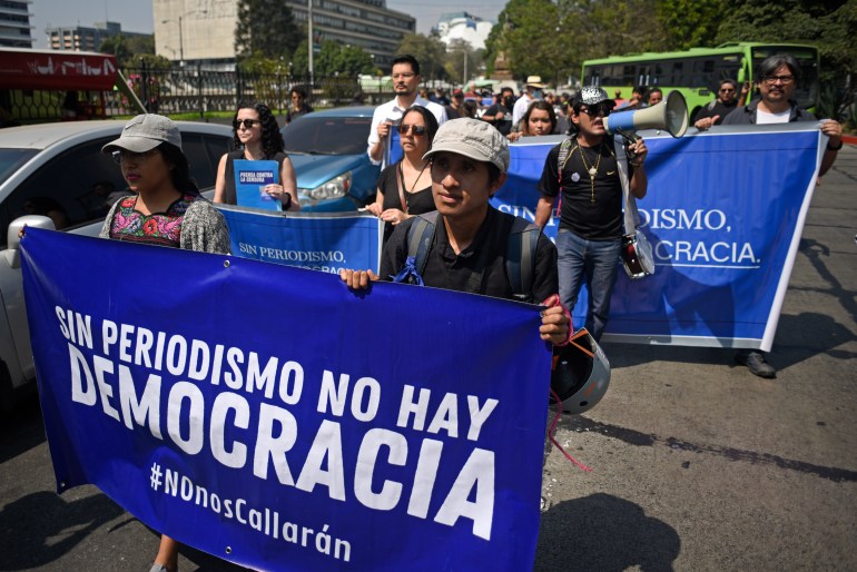 People march outside next to cars holding blue signs and banners, some of which read: “Sin periodismo no hay democracia.”