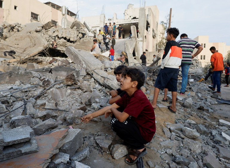 Palestinian children sit amid the rubble as others inspect a building destroyed in Israeli raids in Khan Younis in the southern Gaza Strip