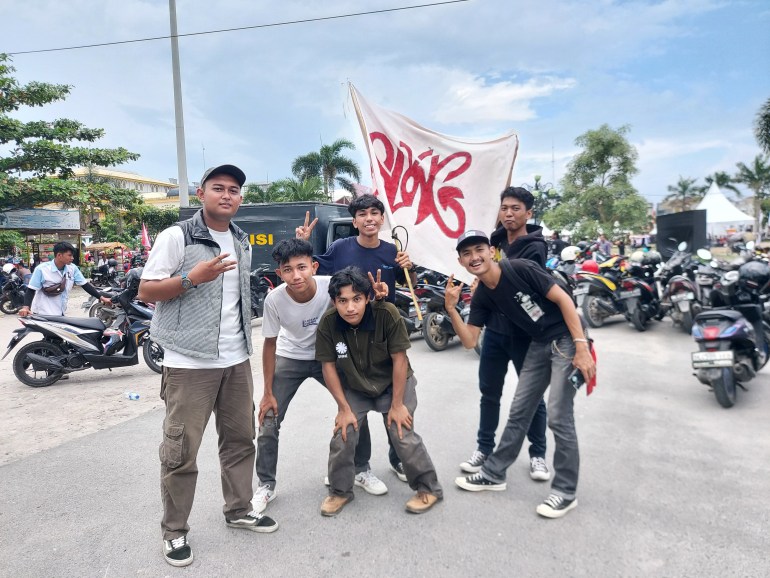 Slank fans outside the venue waving a Slank flag. It is white with a red butterfly-like symbol. The fans are posing. Some are wearing black T-shirts and some white.