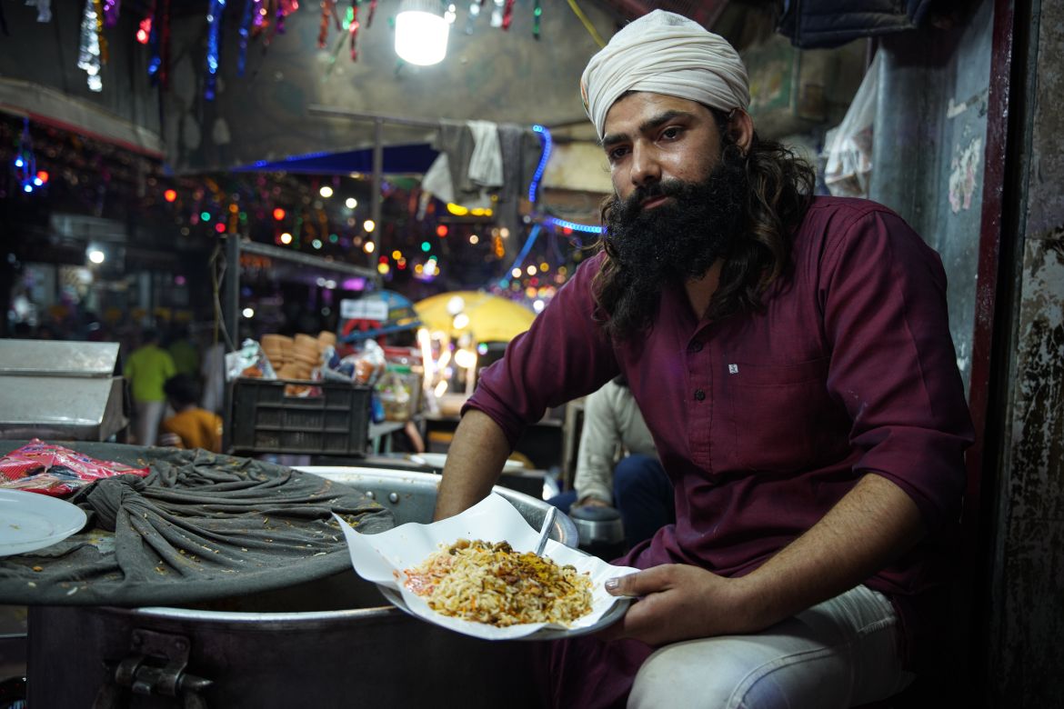 A shopkeeper scoops out biryani from a cooking pot. [Meer Faisal/Al Jazeera]