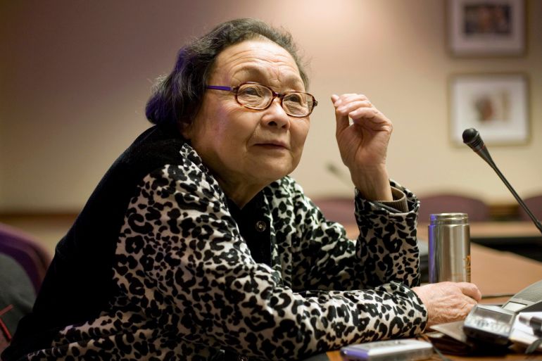 Gao Yaojie. She is pictured at the age of 80. She is seated at a desk. She looks relaxed