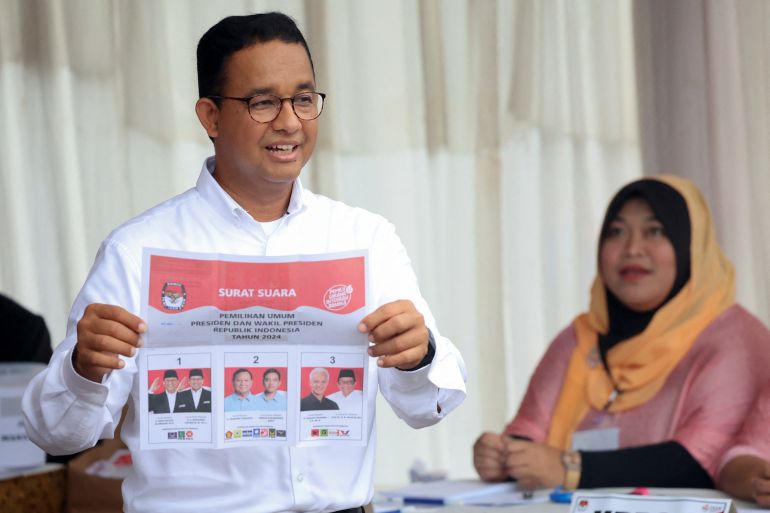 Anies Baswedan holding a ballot paper showing the three main candidate pairs for the election.