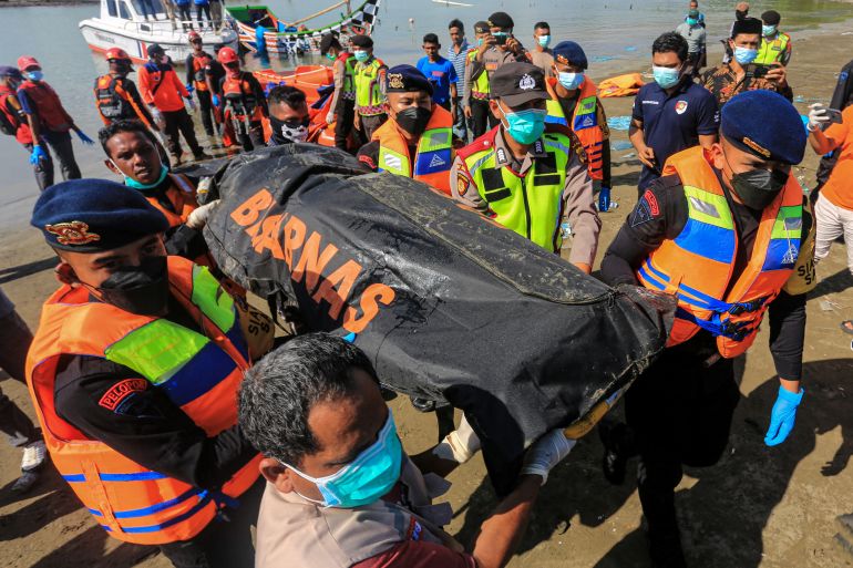 Rescuers in Aceh carrying a black body bag up the beach. The sea is behind them.
