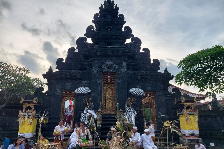 The Balinese temple in Medan. There is a carved stone gateway with wooden doors painted gold. In the steps, women are arranging offerings