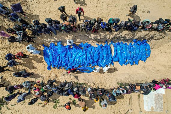 An aerial view shows mourners watching as medical personnel prepare the bodies of 47 Palestinians, that were taken and later released by Israel, during a mass funeral in Rafah in the southern Gaza Strip on March 7, 2024.