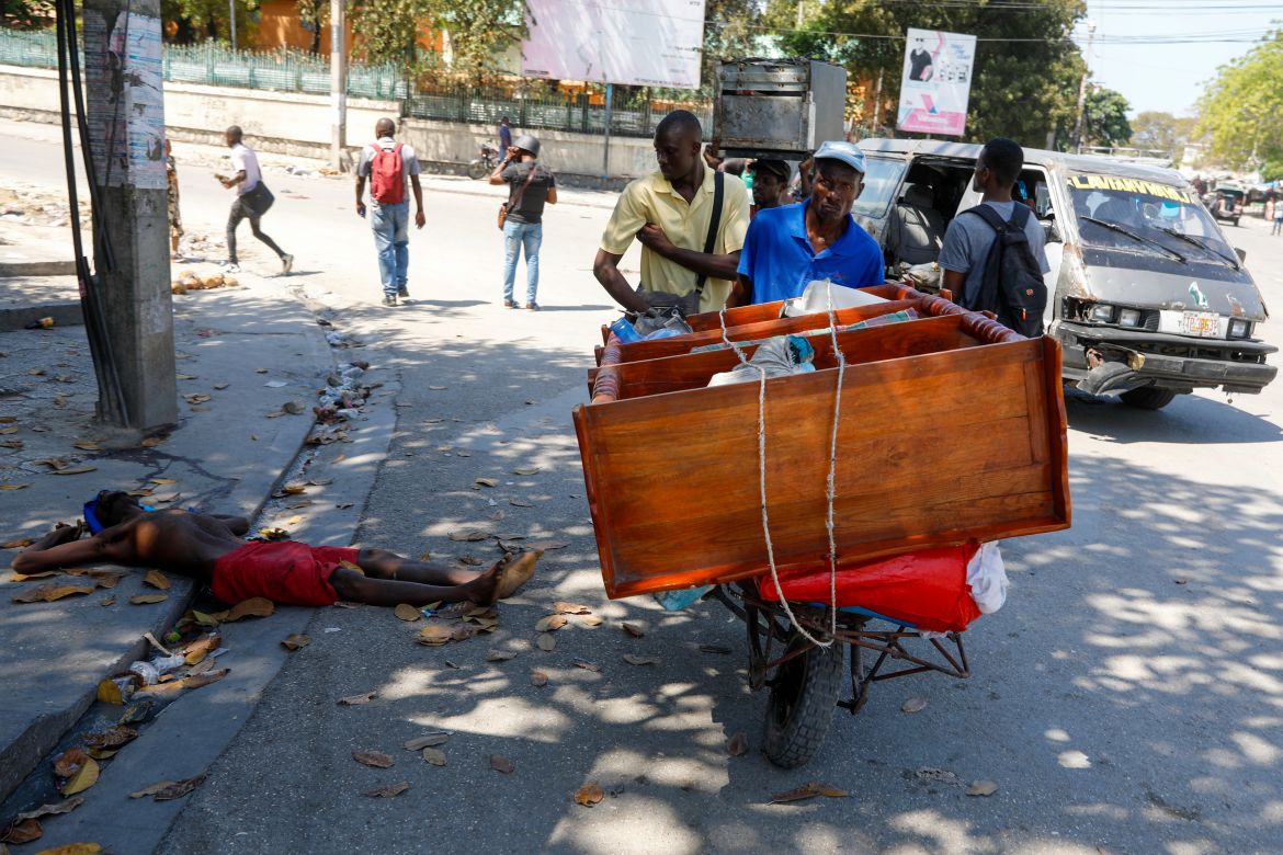 A man pushes a cart past the body of a man shot by unidentified assailants