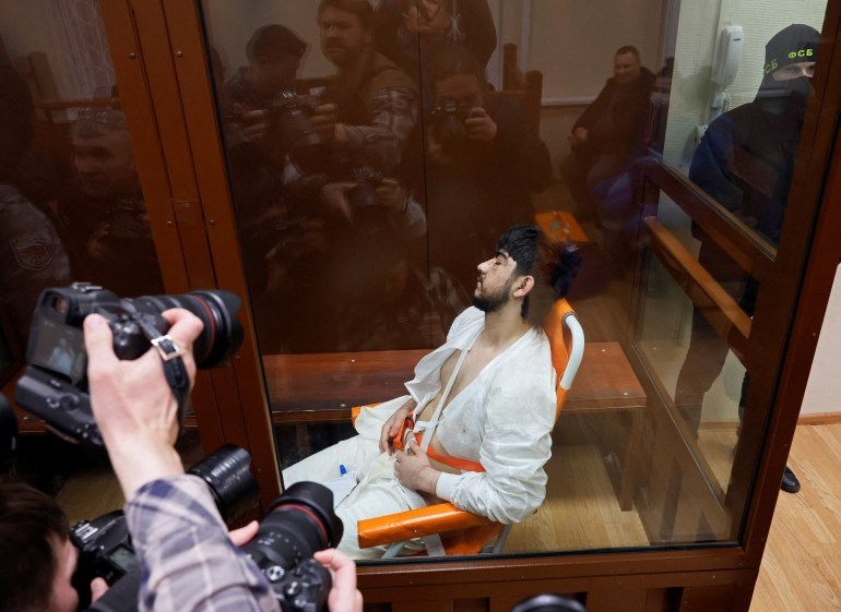 Muhammadsobir Fayzov, suspeito do ataque a tiros na sala de concertos Crocus City Hall, sentado em uma cadeira de transporte médico atrás de uma parede de vidro de um recinto para réus antes de uma audiência no tribunal distrital de Basmanny em Moscou, Rússia, em 25 de março de 2024. REUTERS/Shamil Zhumatov