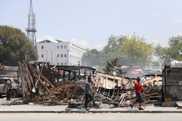 People walk by burnt vehicles in Port-au-Prince, Haiti
