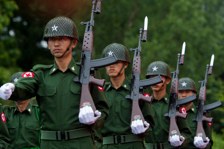 An honour guard of Myanmar soldiers marching. They have their weapons fitted with bayonets on their shoulders. They look serious.