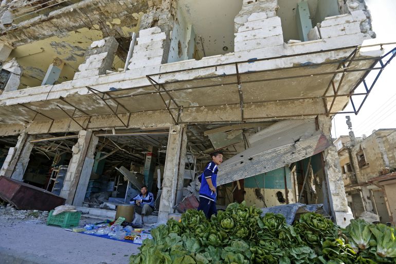 Syrians sell vegetables under a damaged building during the Muslim holy month of Ramadan, in the central city of Homs, on April 28, 2020. / AFP / LOUAI BESHARA RELATED CONTENT