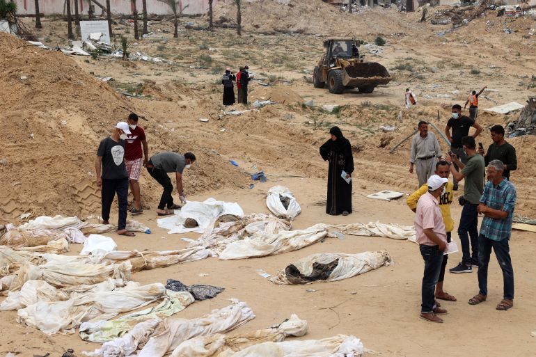 People gather near bodies lined up for identification after they were unearthed from a mass grave found in the Nasser Medical Complex