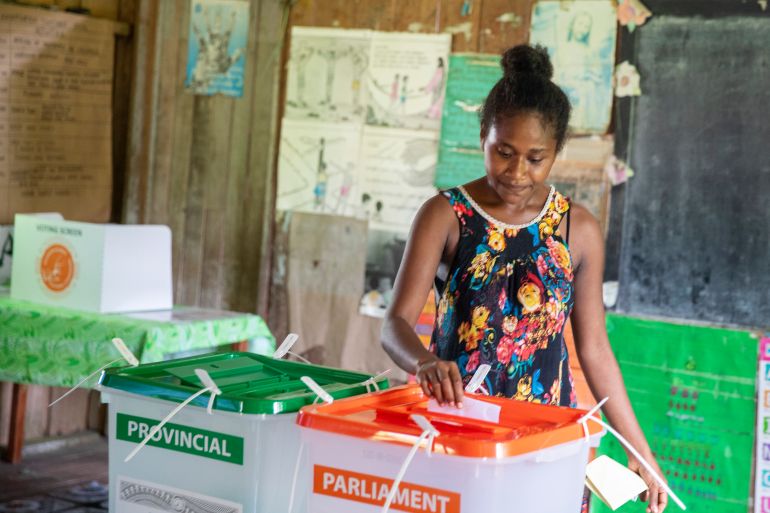 A woman in the Solomon Islands casting her ballot. The clear box for the parliamentary election has an orange lid while the one for the provincial poll has a green lid.