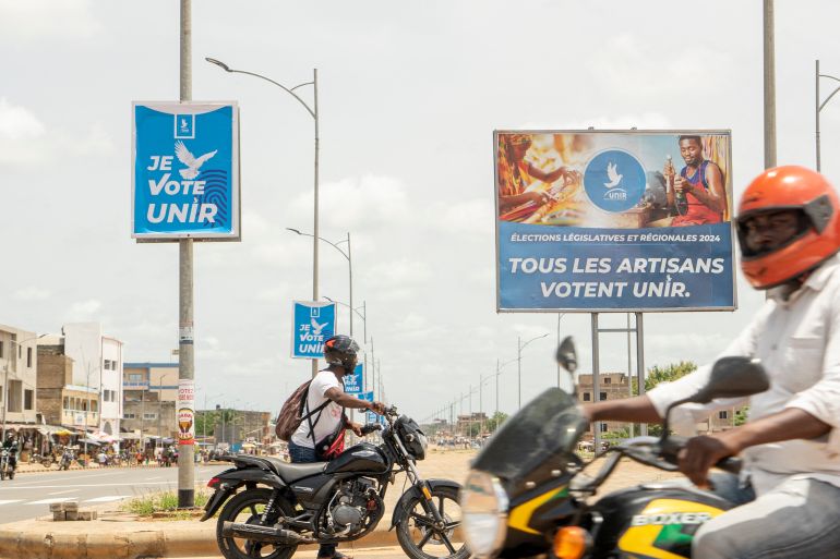 Motorbikes drive past campaign posters in Lome