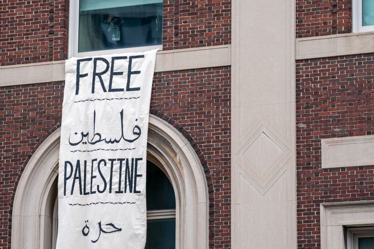 A person stands near a window with a "Free Palestine" banner
