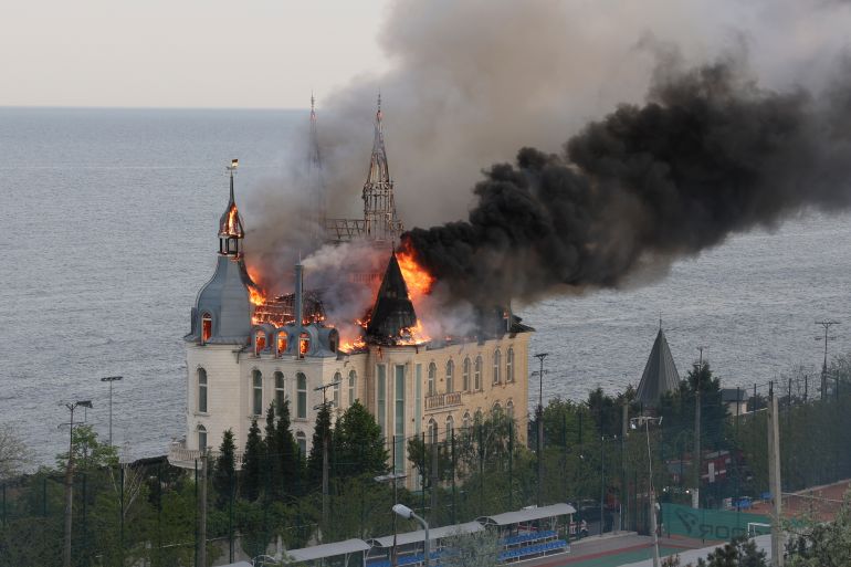 Black smoke and flames billow from the Odesa Law Academy. The building is ornate. The sea is next to the building.