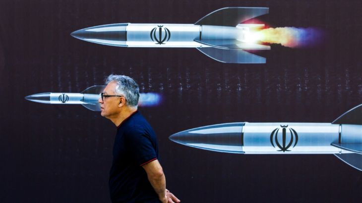 A man walks past a banner depicting missiles along a street in Tehran
