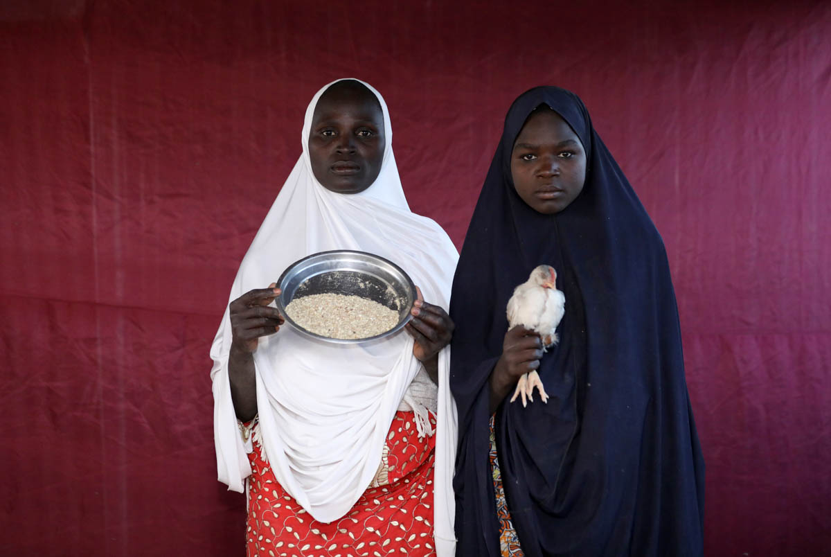 Binta Lawal holds up a bowl of poultry feed with Aisha Buba. [Afolabi Sotunde/Reuters]