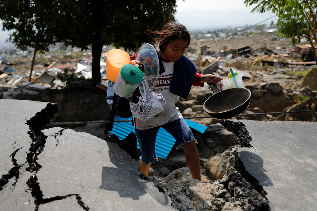 A girl carries valuables from the ruins of her house after the earthquake hit the Balaroa sub-district in Palu. [Beawiharta/Reuters]